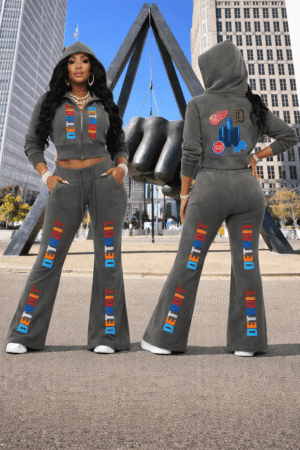 Model wearing a grey vintage-washed cropped fleece hoodie and matching flared sweatpants with colorful “Detroit” text, shown front and back in an urban downtown setting featuring the Joe Louis Fist.